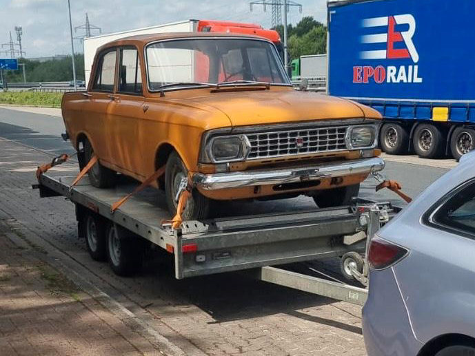 Orangefarbener Oldtimer, mit Spanngurten auf einem Autotrailer gesichert